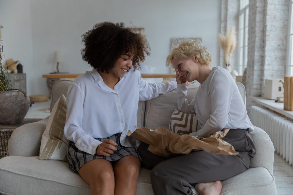 Women sitting on a couch having a casual conversation and smiling.